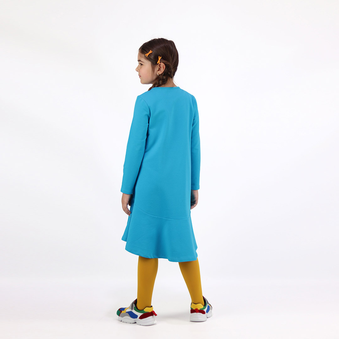 Loose dress is a loose fit dress, that goes wider to the bottom. It is longer on the back with a wide frilled trim at the bottom. Dress is in blue colour. Children, 3 -10 yrs. BonnyJoy - wearing, on the back