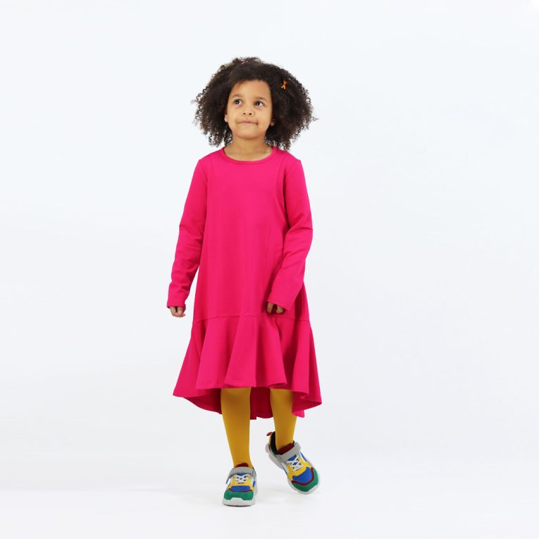 Loose dress is a loose fit dress, that goes wider to the bottom. It is longer on the back with a wide frilled trim at the bottom. Dress is in raspberry colour. Children, 3 -10 yrs. BonnyJoy -wearing, in front