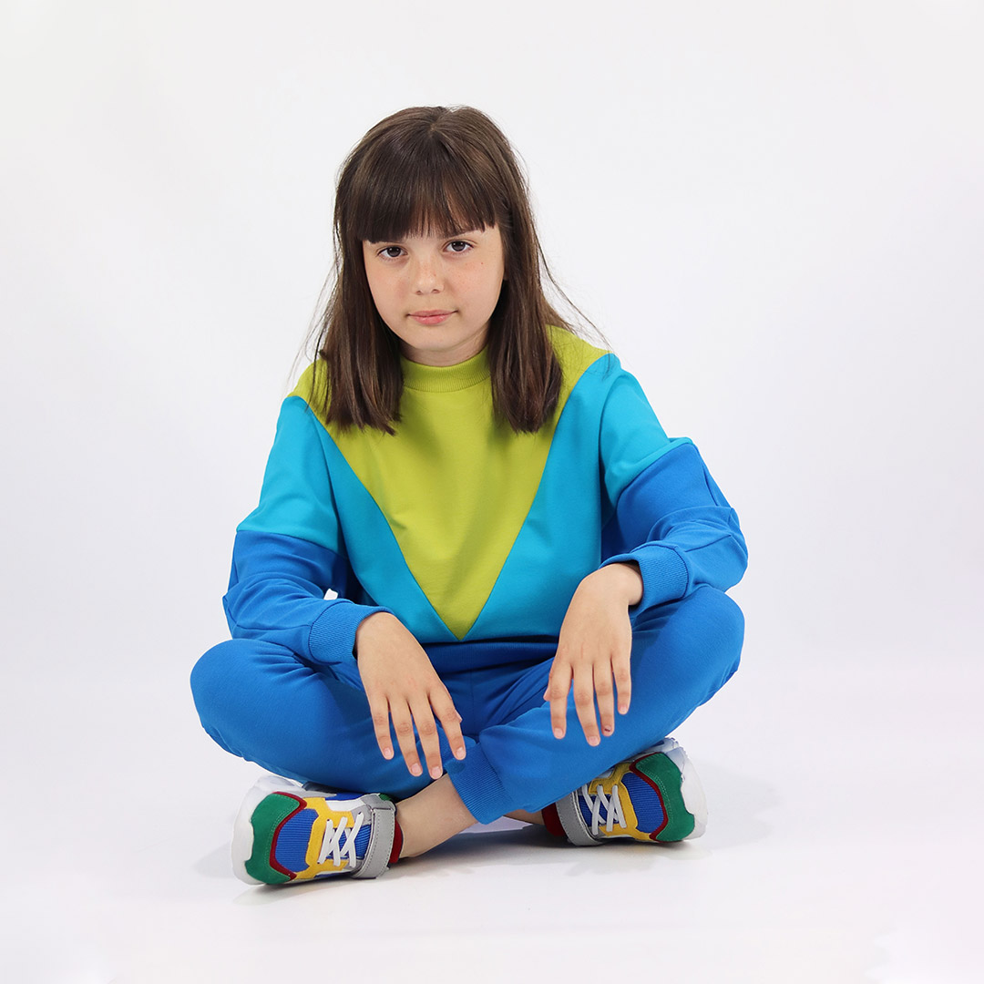 Batwing sweatshirt is a loose fit top with triangular form color blocks. It comes in a combo of three colours - bright lime, electric blue and deep blue. Front view, sitting. Children, 3 -10 yrs. BonnyJoy