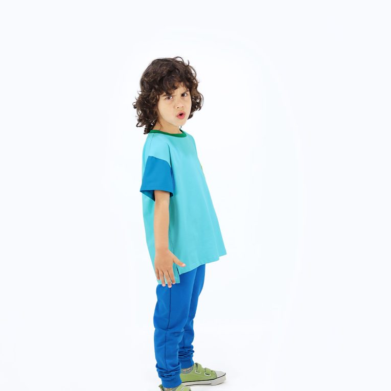Our colour block t-shirt is a loose fit top with square pocket on the left and a little longer on the back. The front and the back in blue colour, right sleeve in electric blue, left sleeve and the pocket - in bright lime. On the neck - green colour. Side view. Children, 3 -10 yrs. BonnyJoy