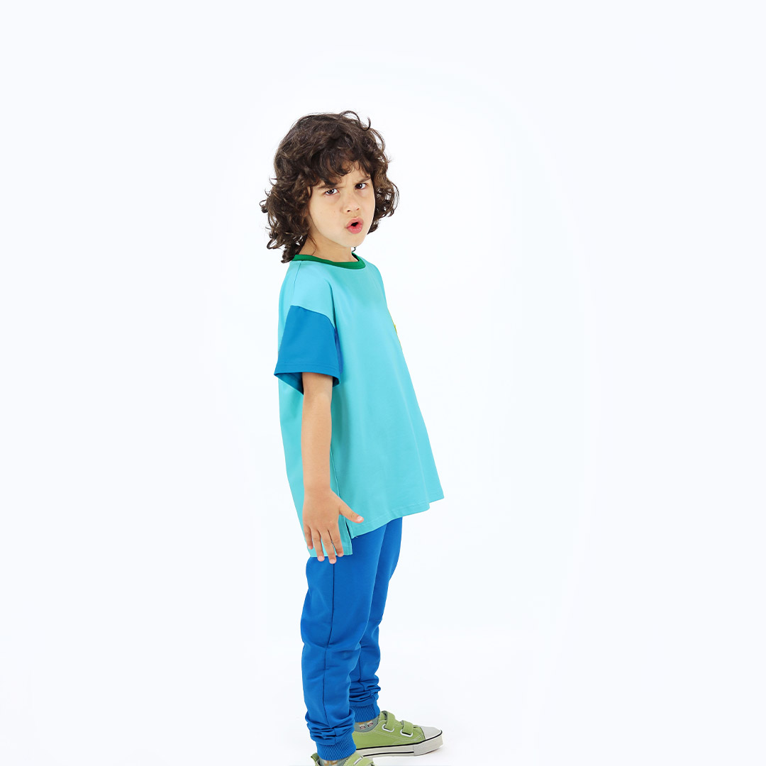 Our colour block t-shirt is a loose fit top with square pocket on the left and a little longer on the back. The front and the back in blue colour, right sleeve in electric blue, left sleeve and the pocket - in bright lime. On the neck - green colour. Side view. Children, 3 -10 yrs. BonnyJoy