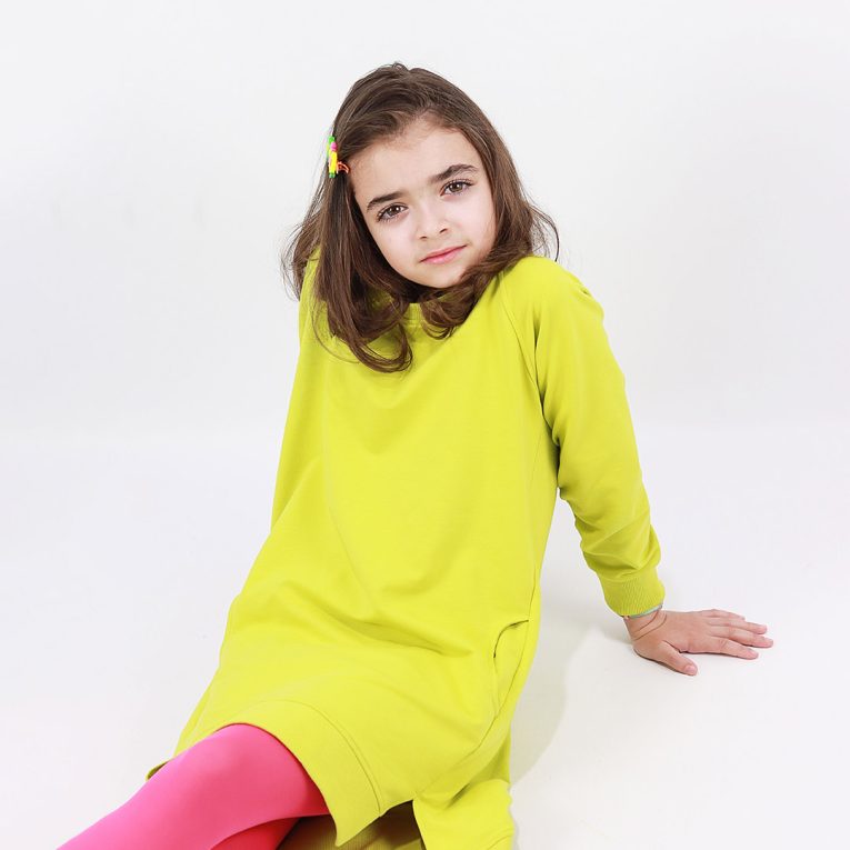 Cylinder dress is a one-colour loose fit dress with round pockets aside and a little longer on the back in bright lime colour. Front view, closer look. Children, 3 -10 yrs. BonnyJoy