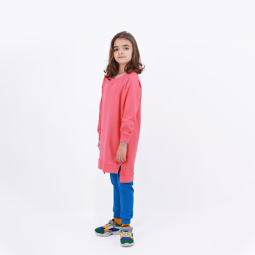 Cylinder dress is a one-colour loose fit dress with round pockets aside and a little longer on the back in salmon colour. Side view. Children, 3 -10 yrs. BonnyJoy