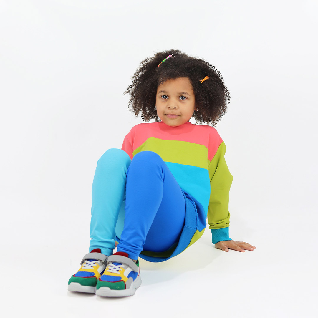 Four-Colour Sweatshirt is a regular fit top with colour block design. Right arm and the top part - salmon, left arm and the chest part - bright lime, belly part - electric blue, bottom part and the ribbed bottom hem - deep blue. The ribbed hand cuffs on the right is bright lime, on the left is electric blue. Front view, a girl sitting. Children, 3 -10 yrs. BonnyJoy