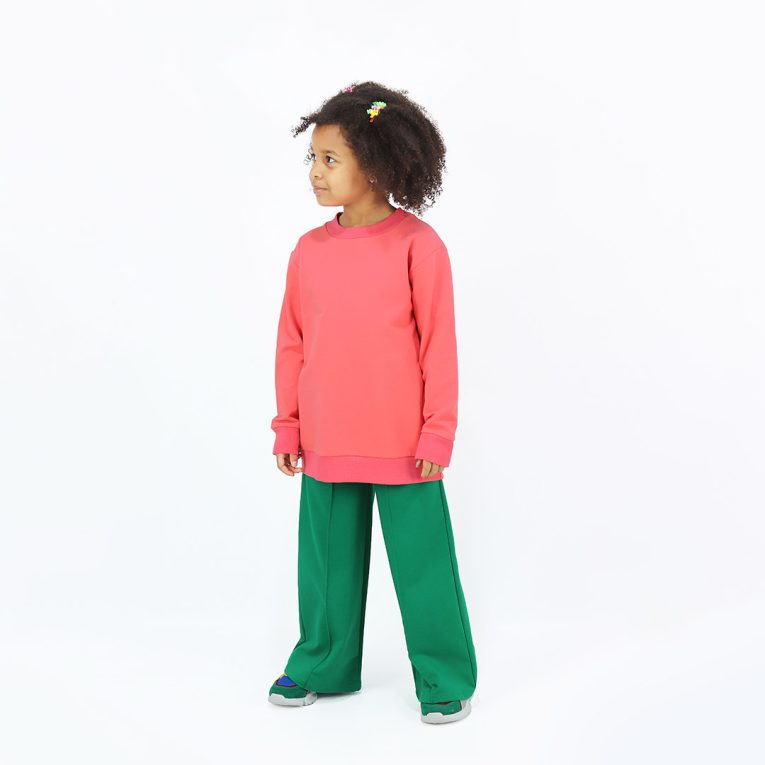 Joyful Sweatshirt is a loose fit top with minimalist design in salmon colour that features a ribbed neck, sleeve ends and bottom hem. Front view, a girl standing. Children, 3 -10 yrs. BonnyJoy