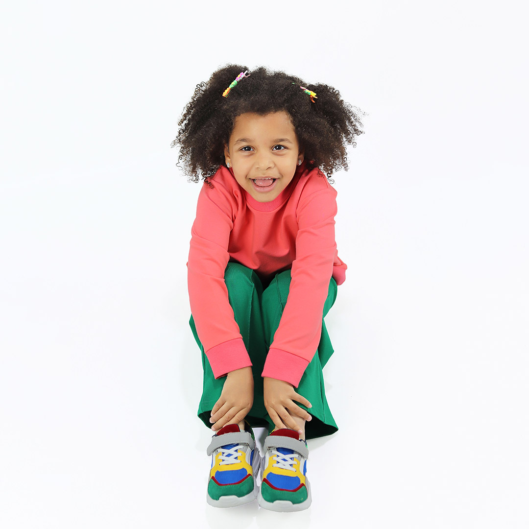 Joyful Sweatshirt is a loose fit top with minimalist design in salmon colour that features a ribbed neck, sleeve ends and bottom hem. Front view, a girl sitting. Children, 3 -10 yrs. BonnyJoy