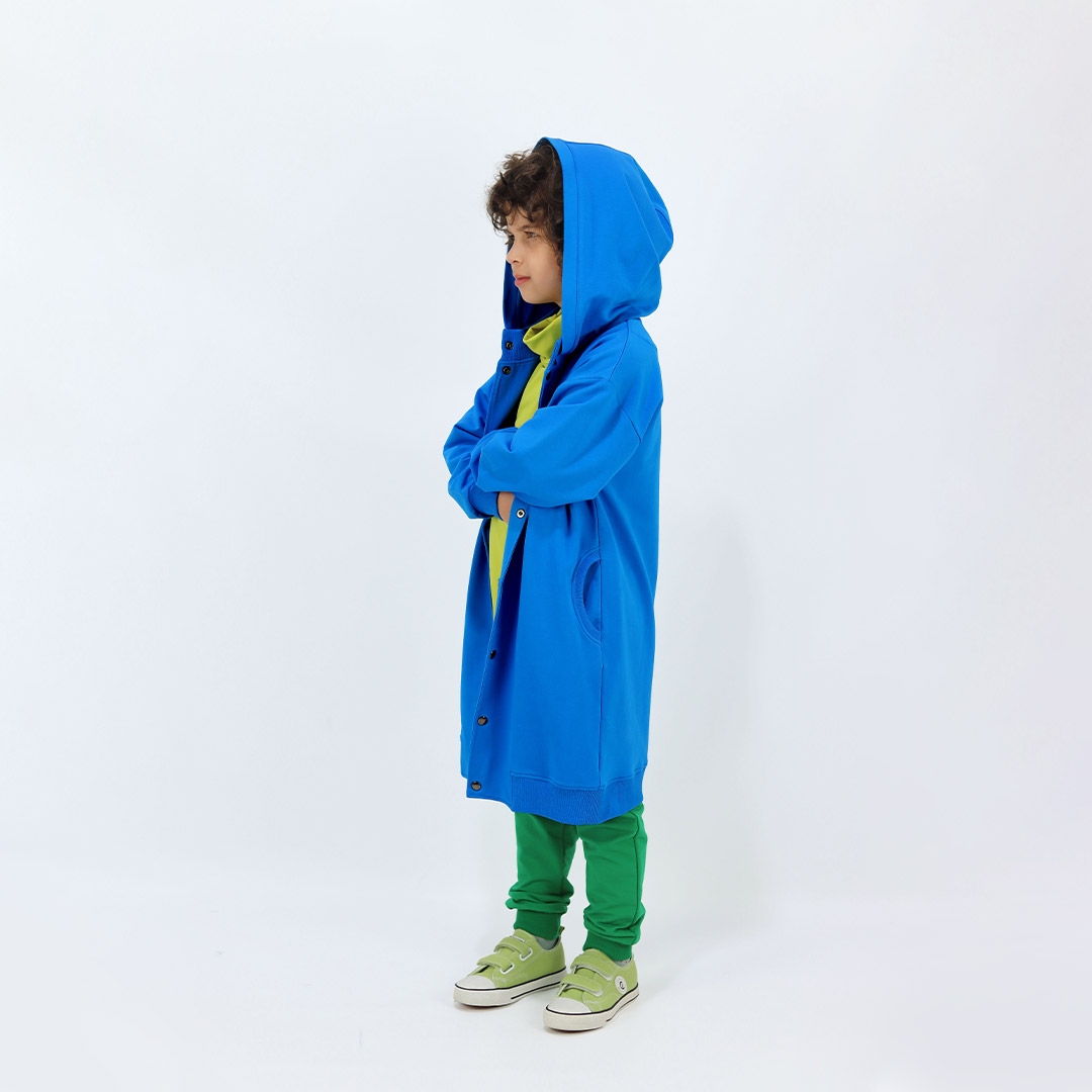 Long buttoned hoodie has a straight loose fit and minimalist design in deep blue colour. It closes up with snap buttons and features hign ribbed neck and ribbed hand cuffs and bottom hem. Side view, the hood on. Children, 3 -10 yrs. BonnyJoy