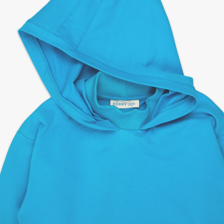 Long hoodie with high ribbed neck in electric blue colour. It features ribbed hand cuffs and a kangaroo pocket. The hoodie is a little longer on the back. Front view, close-up. Children, 3 -10 yrs. BonnyJoy