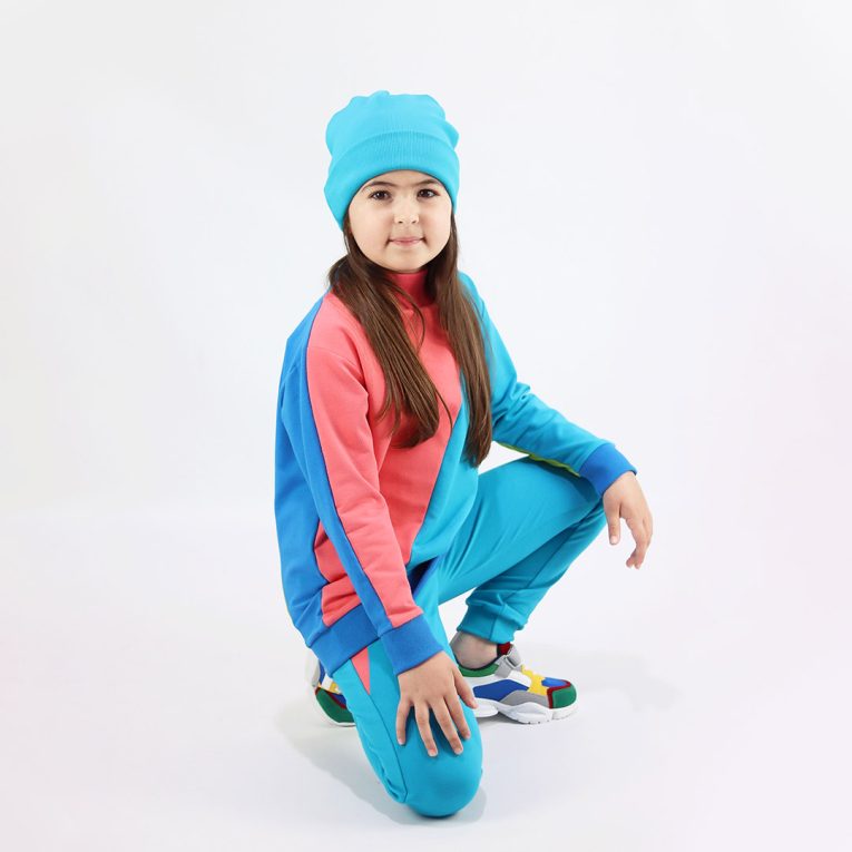 Slim Fit Colour Block Joggers are a pair of sweatpants in electric blue with two Italian type side pockets in different colours - salmon and bright lime. It features ribbed waist and cuffs. Front view, a girl sitting. Children, 3 -10 yrs. BonnyJoy