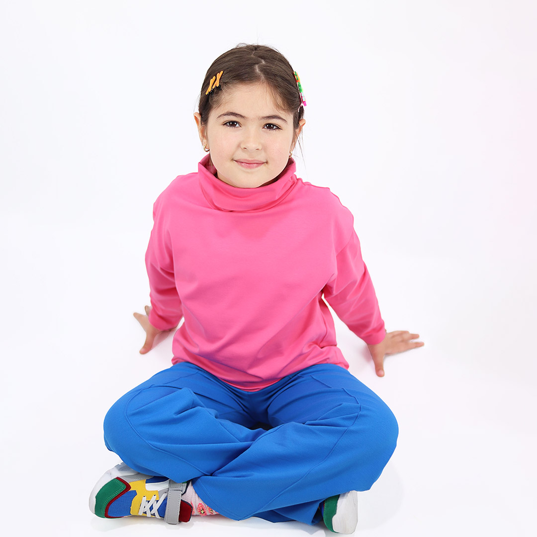 Turtleneck loose top is a classic top loose on the neck in pink colour. Front view, a girl sitting. Children, 3 -10 yrs. BonnyJoy