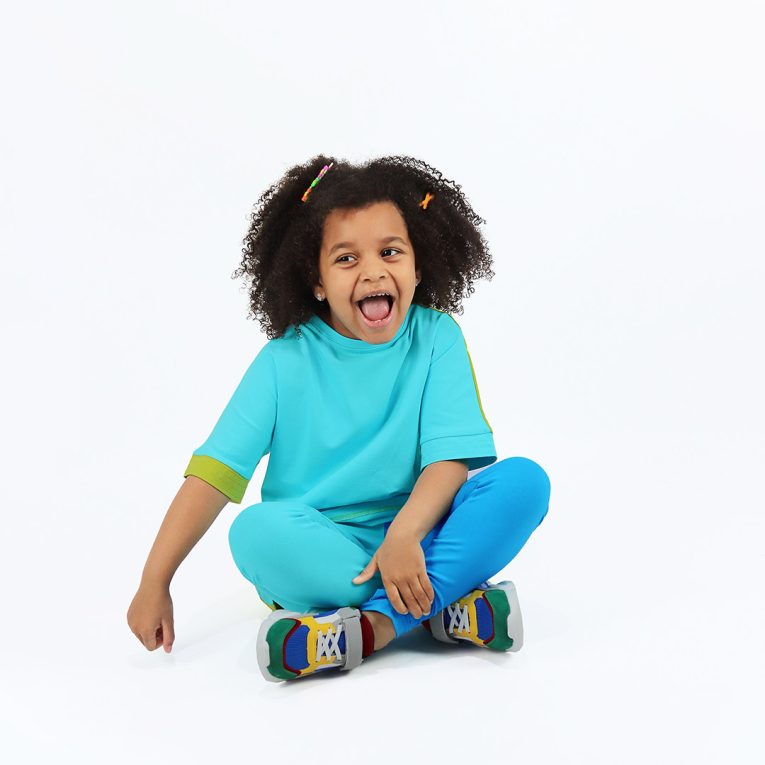 Our two-way top is a loose fit top with short sleeves in two colours. On one side is bright lime, on the other - blue colour. You could wear it front on the back and the other way round. Blue in front, a girl sitting. Children, 3 -10 yrs. BonnyJoy