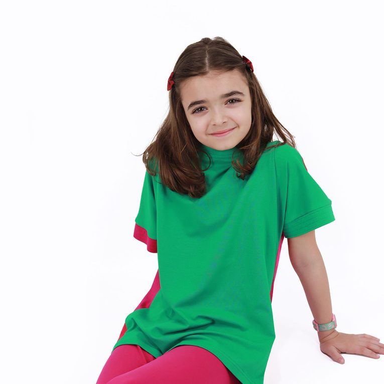 Our two-way top is a loose fit top with short sleeves in two colours. On one side is raspberry, on the other - green colour. You could wear it front on the back and the other way round. Green in front, a girl is sitting. Children, 3 -10 yrs. BonnyJoy