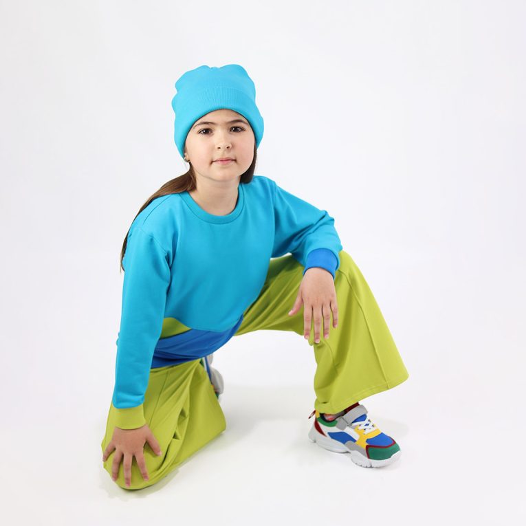Wide leg pants with an edge hem in front and ribbed waist. Loose fit pants in bright lime colour. Front view, a girl sitting. Children, 3 -10 yrs. BonnyJoy