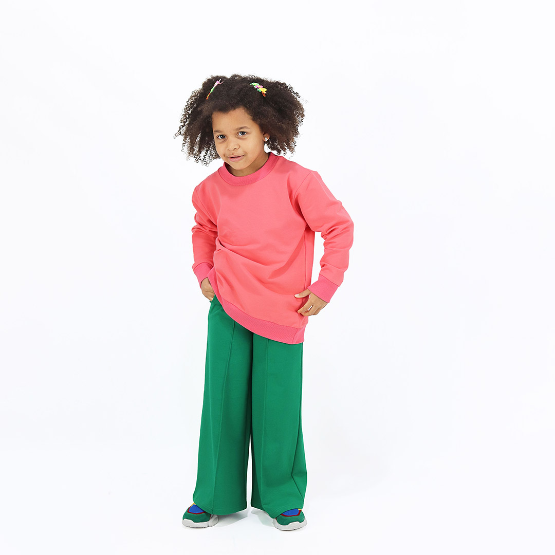 Wide leg pants with an edge hem in front and ribbed waist. Loose fit pants in green colour. Front view, a girl standing. Children, 3 -10 yrs. BonnyJoy