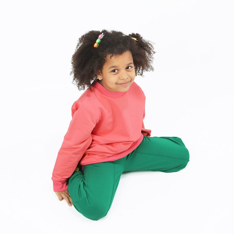 Wide leg pants with an edge hem in front and ribbed waist. Loose fit pants in green colour. Front view, a girl sitting. Children, 3 -10 yrs. BonnyJoy